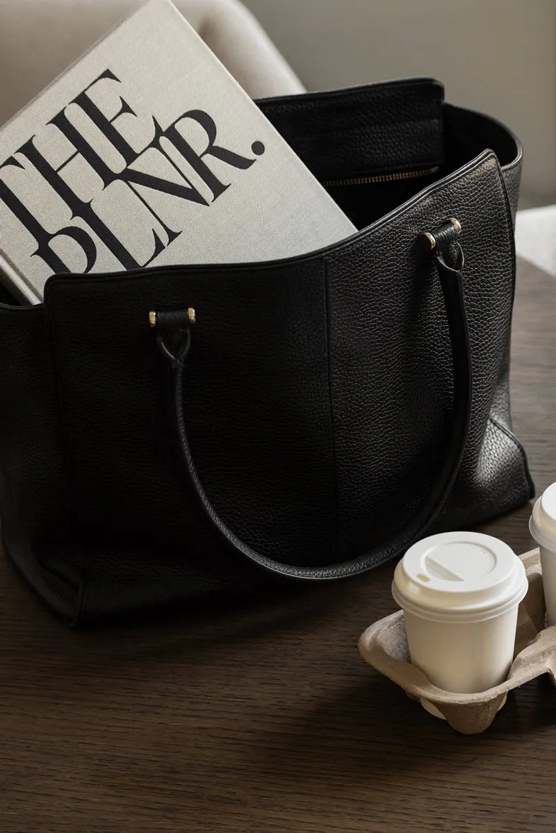 The PLNR in a leather bag on a dark oak table with two takeaway cups of espresso