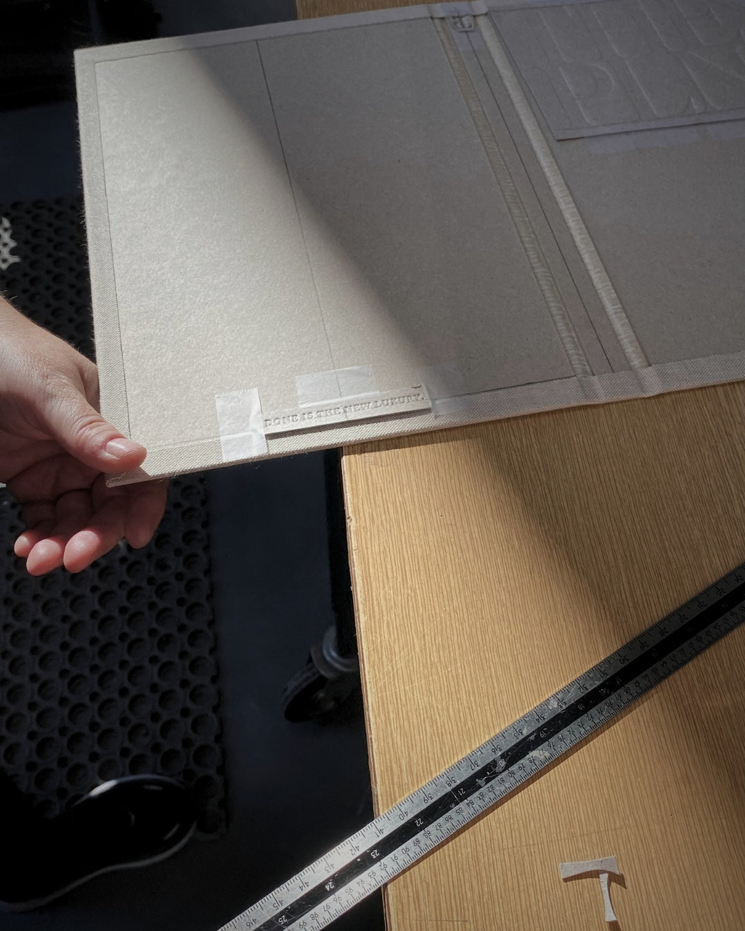 Person holding a textured rectangular object on a wooden surface with a ruler in the foreground. The making of THE PLNR in Norway - the template for embossing